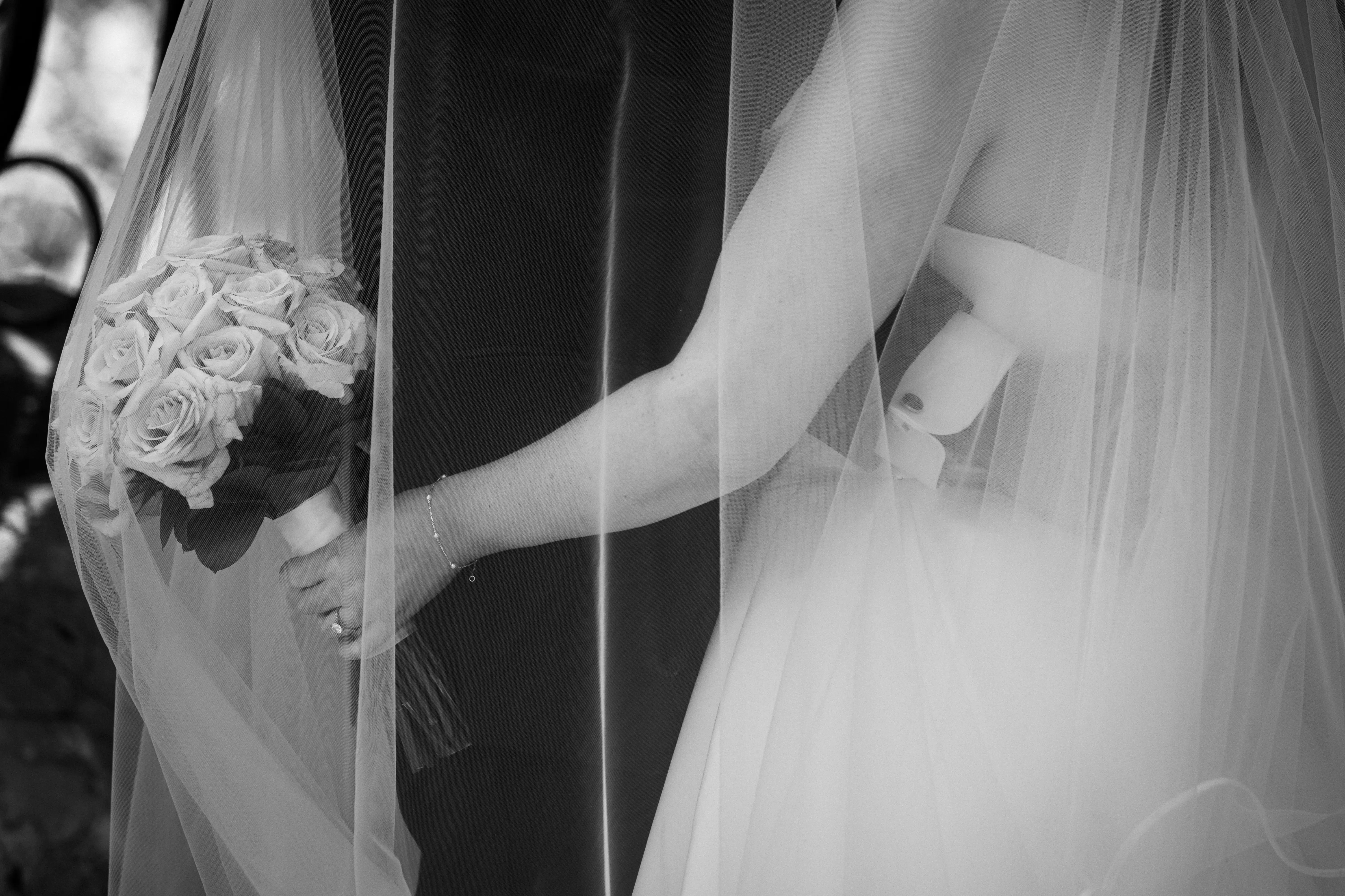 Un voile transparent tombe sur un bouquet de roses près d’un bras portant un bracelet fin.
